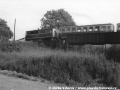 Osobní vlak vedený motorovou lokomotivou T 47.008 právě přejíždí železniční most přes tratě velké železnice do Černous a Jindřichovic pod Smrkem | 28.5.1975