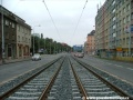 Středem Plzeňské ulice na zvýšeném tělese pokračuje tramvajová trať v klesání.