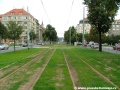 Tramvajová trať klesá v přímém úseku ve středu ulice Jugoslávských partyzánů v zatravněné podobě kolejiště.