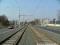 Za přejezdem u Chvalské ulice se protisměrné tramvajové koleje sbližují a sloupy trolejového vedení se ocitají na kraji tramvajového tělesa.