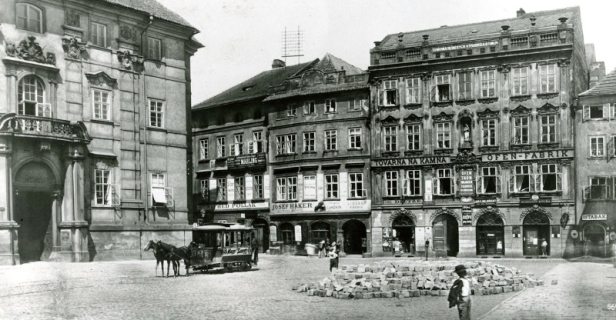 Před budovou Klementina na Mariánském náměstí snímek zachycuje vůz koňky, který právě přijel Platnéřskou ulicí od Karlova mostu. Koňka zde byla provozována v letech 1883 - 1901, pak došlo k elektrifikaci tratě. Na Mariánském náměstí dochází k dokončování dláždění a v prostoru dnešní Ústřední městské knihovny ještě stojí blok původních domů. | mezi 1883 - 1901